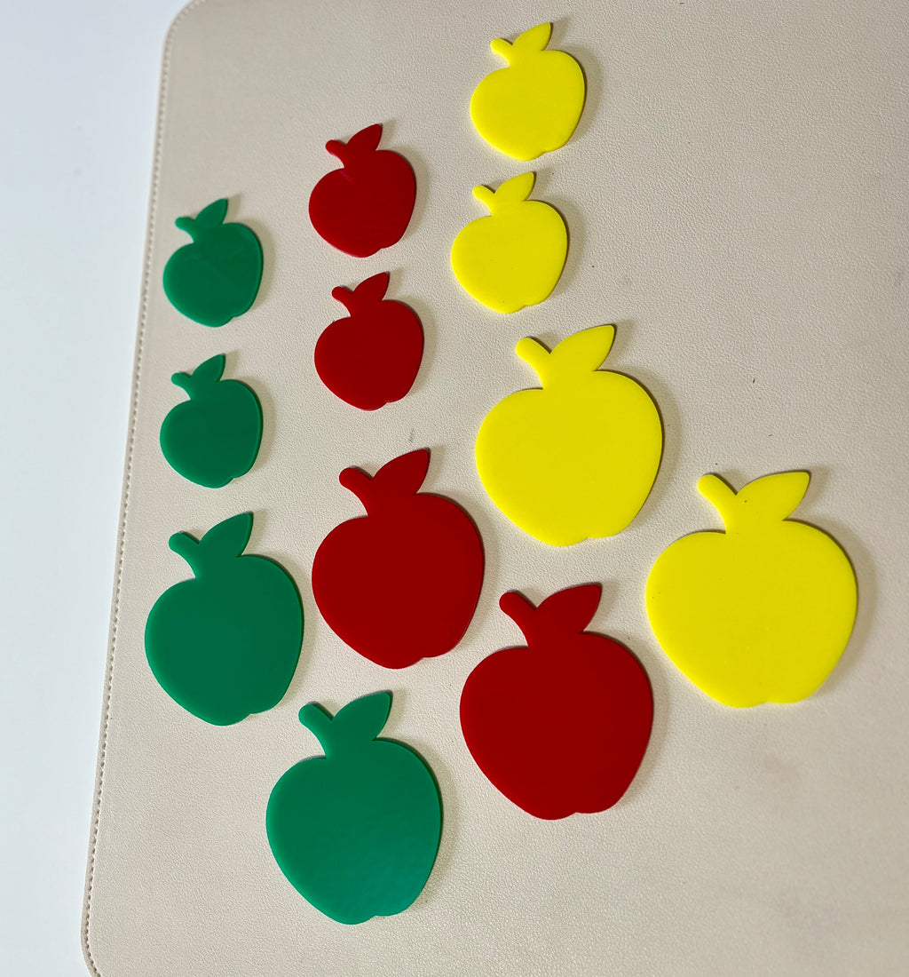 Green, red, and yellow apple-shaped pieces in three different sizes arranged on a light surface