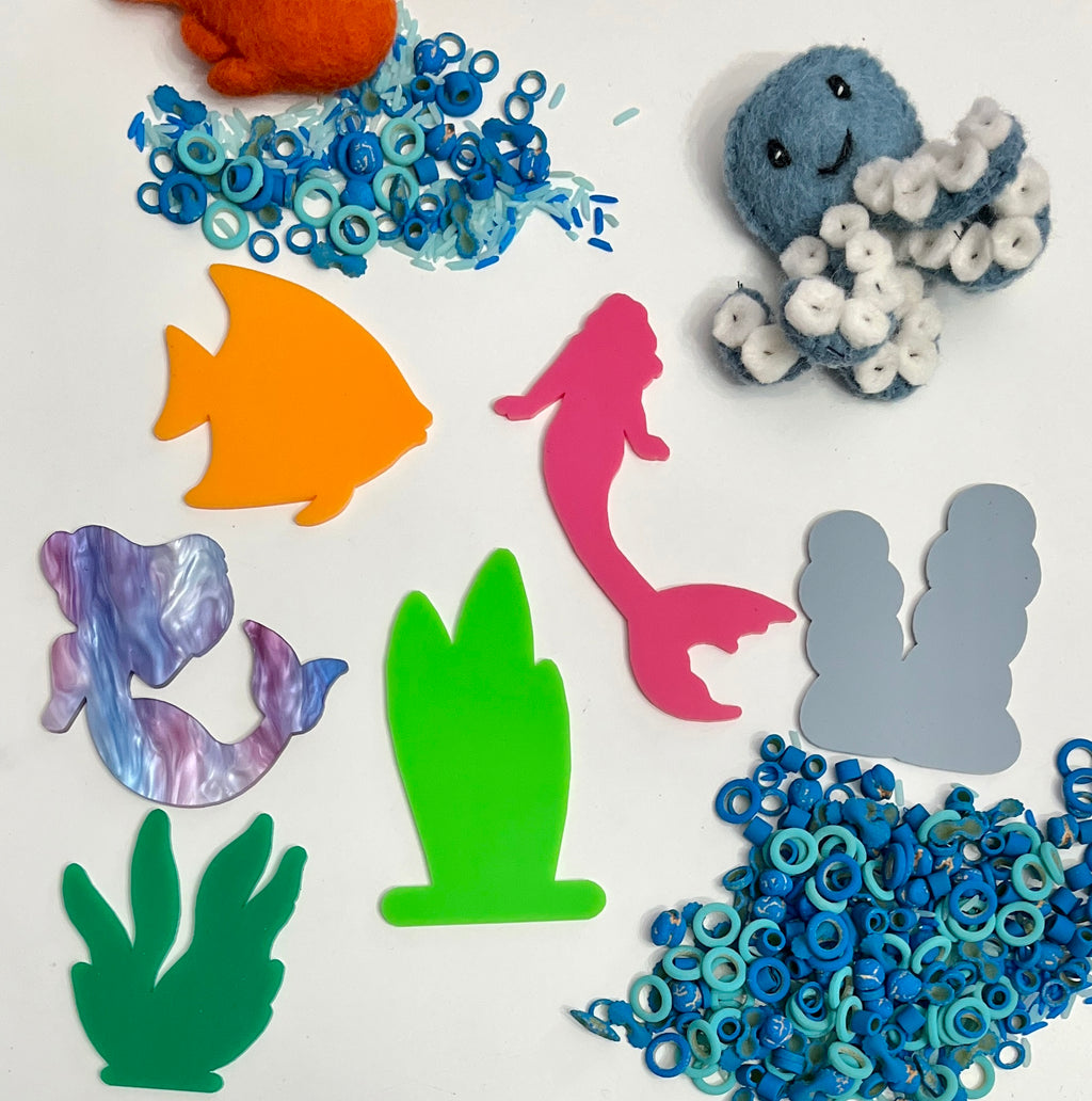 Felt orange crab, blue felt octopus with white suckers, colorful acrylic sea shapes, and small blue sea ring pieces on white surface