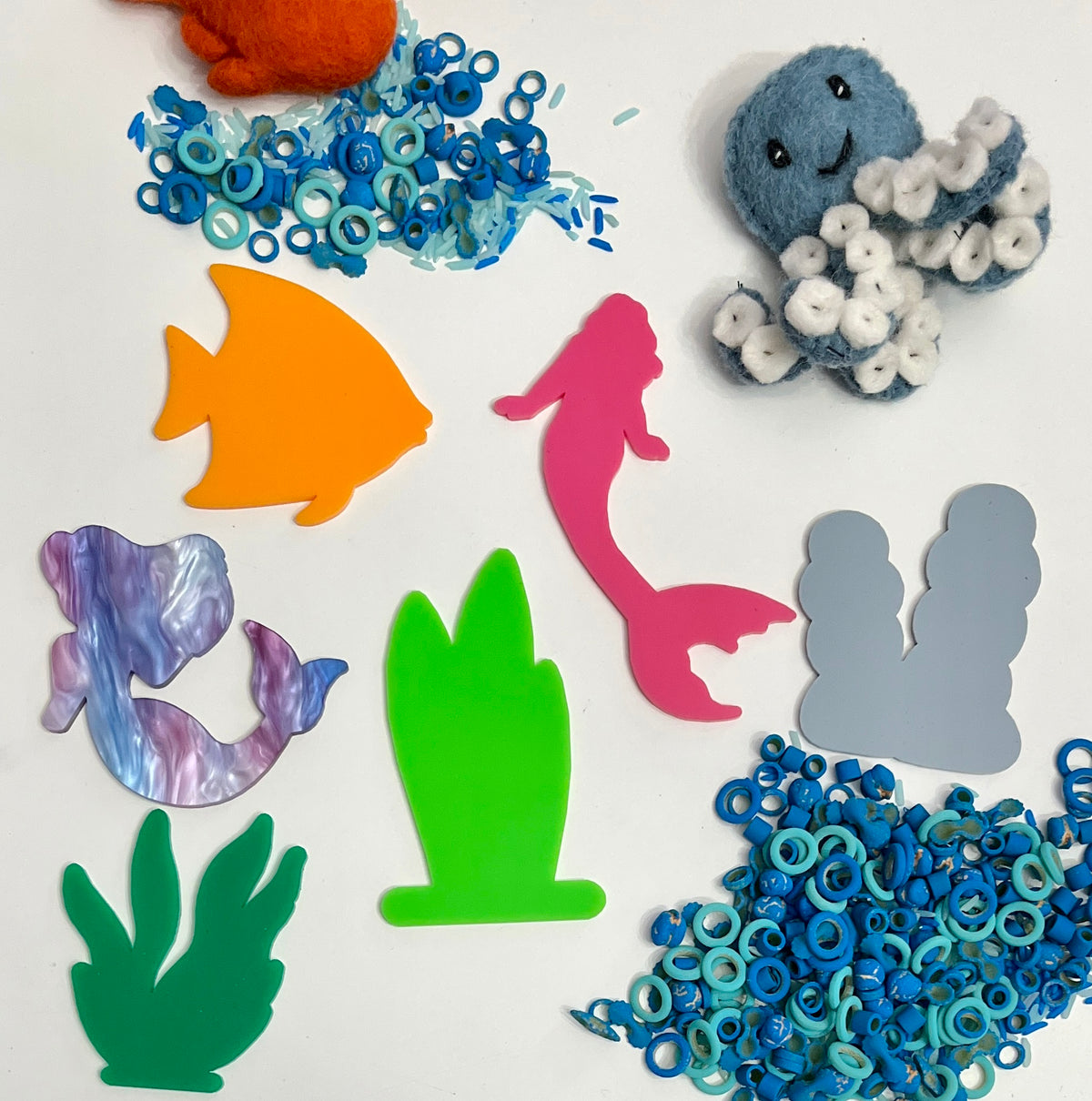 Felt orange crab, blue felt octopus with white suckers, colorful acrylic sea shapes, and small blue sea ring pieces on white surface