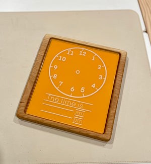 Wood-framed orange learning clock board with white numbers and space to write time, am, and pm options