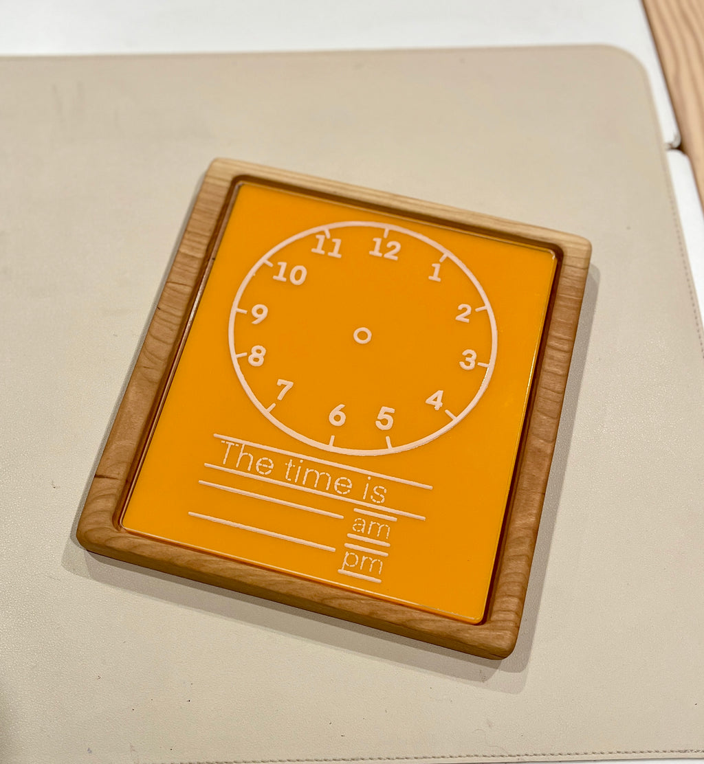 Wood-framed orange learning clock board with white numbers and space to write time, am, and pm options