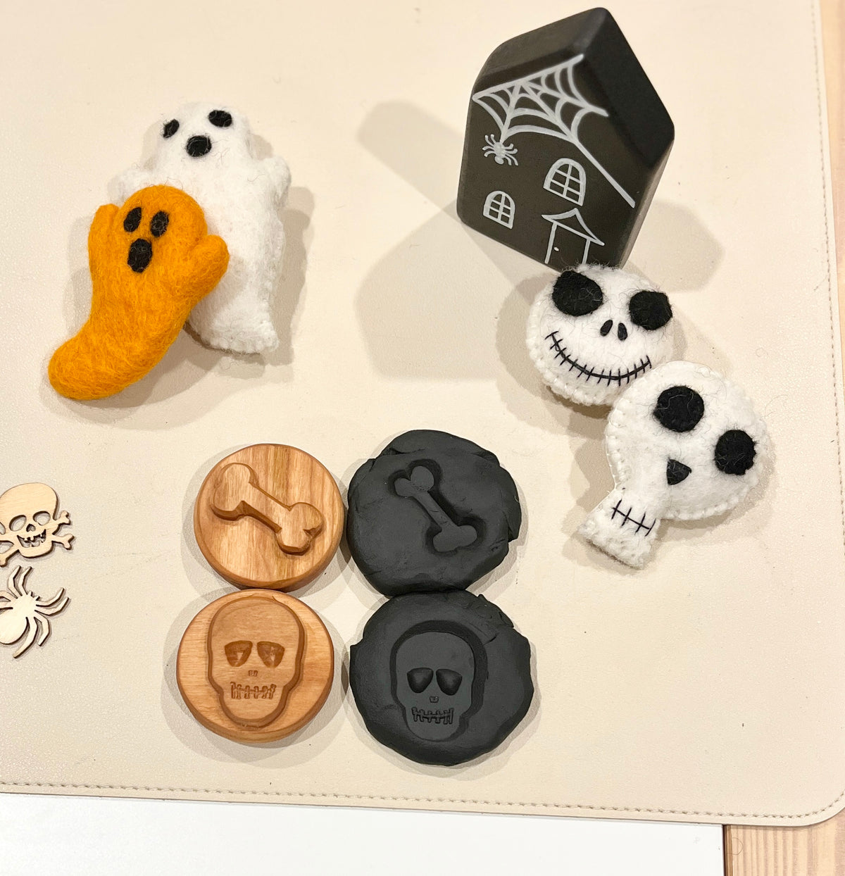 Felt ghosts and skulls with stitched faces, wooden and black tokens engraved with bones and skulls, and a black haunted house figure with a spiderweb design