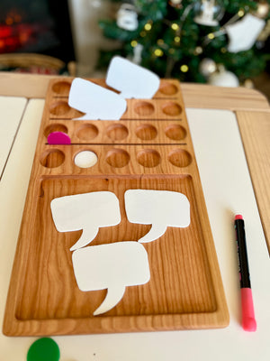 Wooden organizer tray with circular slots and blank white speech bubble cards alongside a pink marker on white table