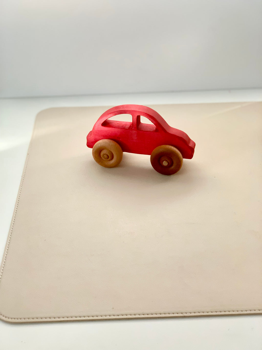 Red wooden toy car with natural wood wheels placed on a smooth beige surface in soft lighting