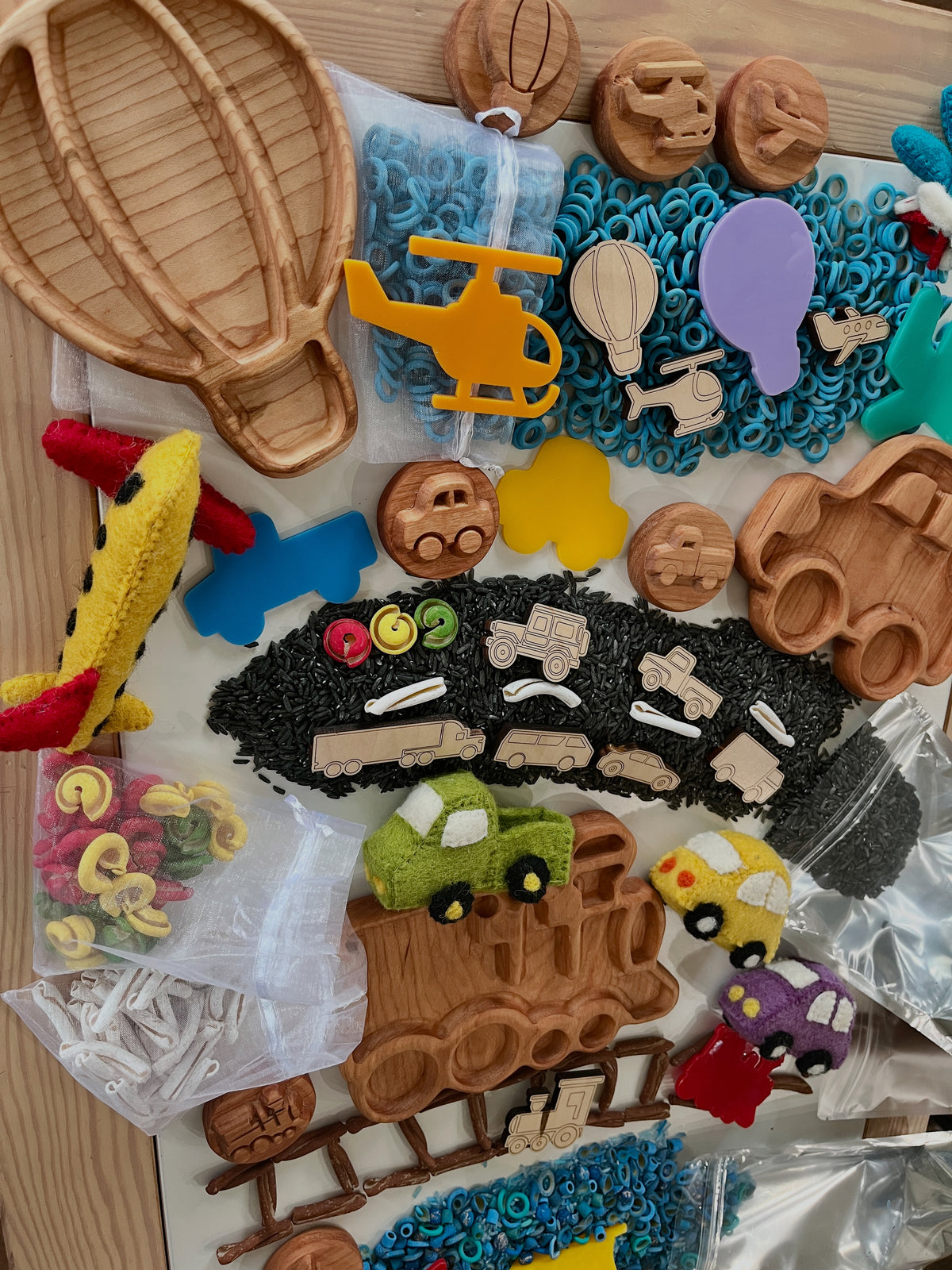 Wooden and felt vehicle-themed trays, stamps, and colorful rice pieces arranged on wooden surface with toy vehicles.