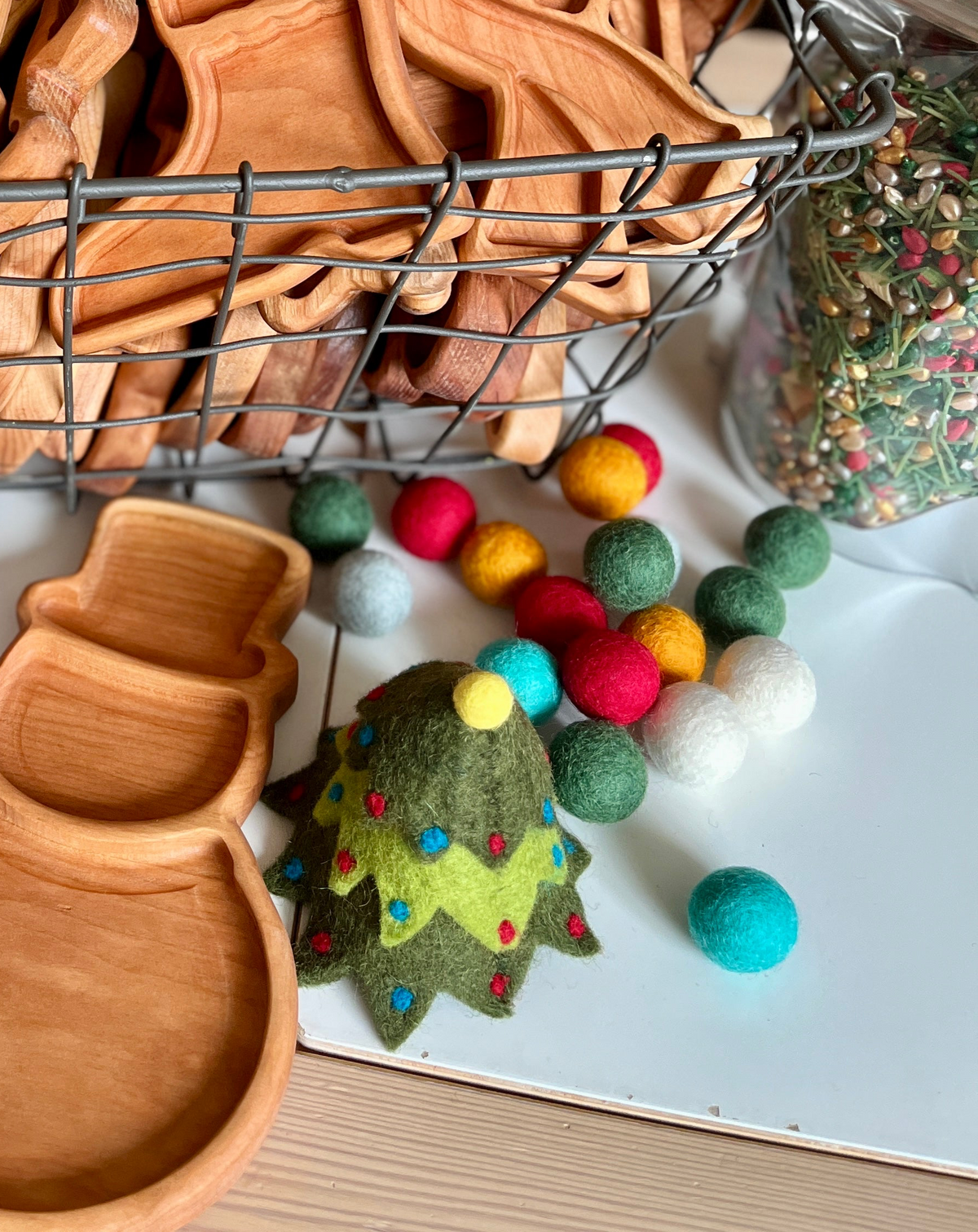 Wooden snowman-shaped trays with colorful felt balls and a felt Christmas tree decoration on white surface