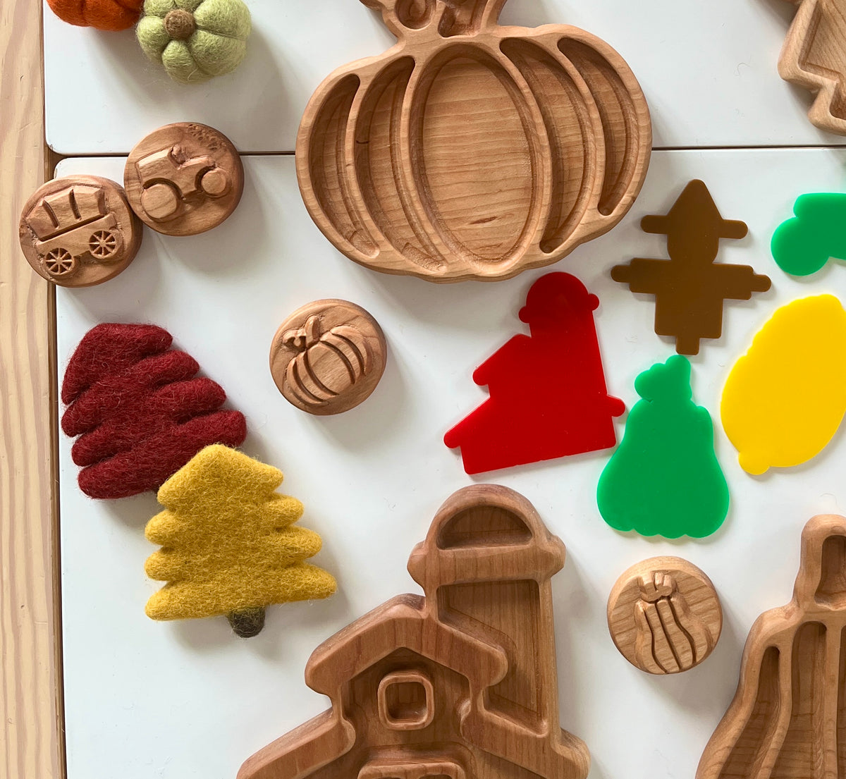 Wooden pumpkin tray, small wooden tokens with fall designs, colorful felt trees, and autumn-themed acrylic shapes on white surface