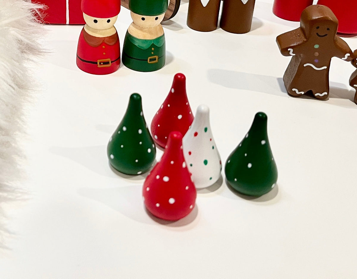 Small red, green, and white cone-shaped wooden decorations with white polka dots on white surface