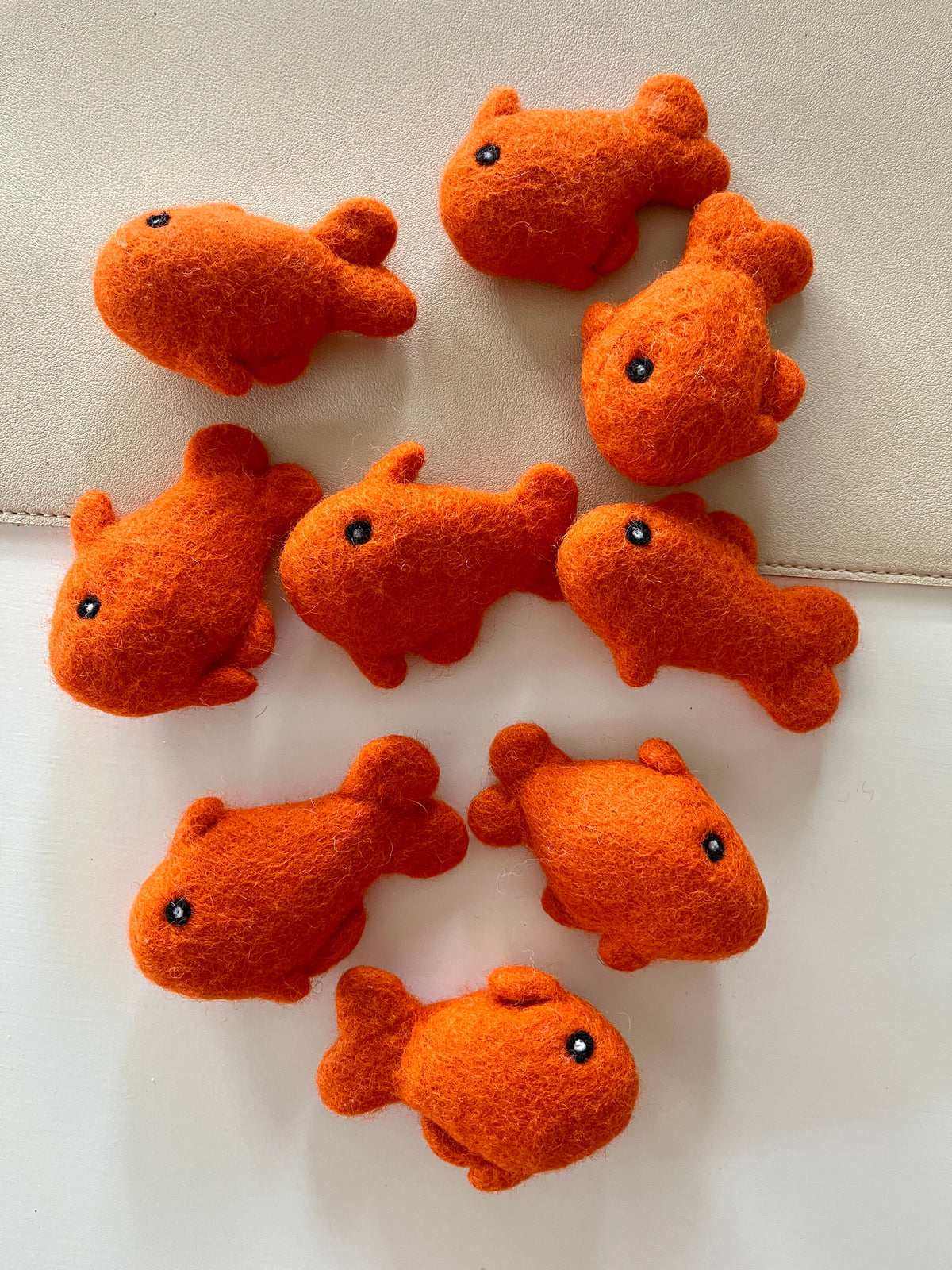 Eight small bright orange felt fish with black eyes arranged on a light surface and beige background