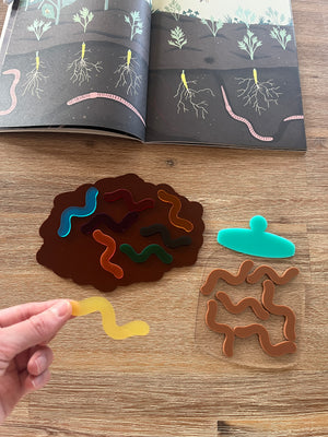 Little Dry Erasables - Worms with Dirt or Jar showing colorful translucent worm shapes on a brown dirt-shaped tray, a clear jar piece, and a hand holding a yellow worm, handcrafted homeschool education resources.