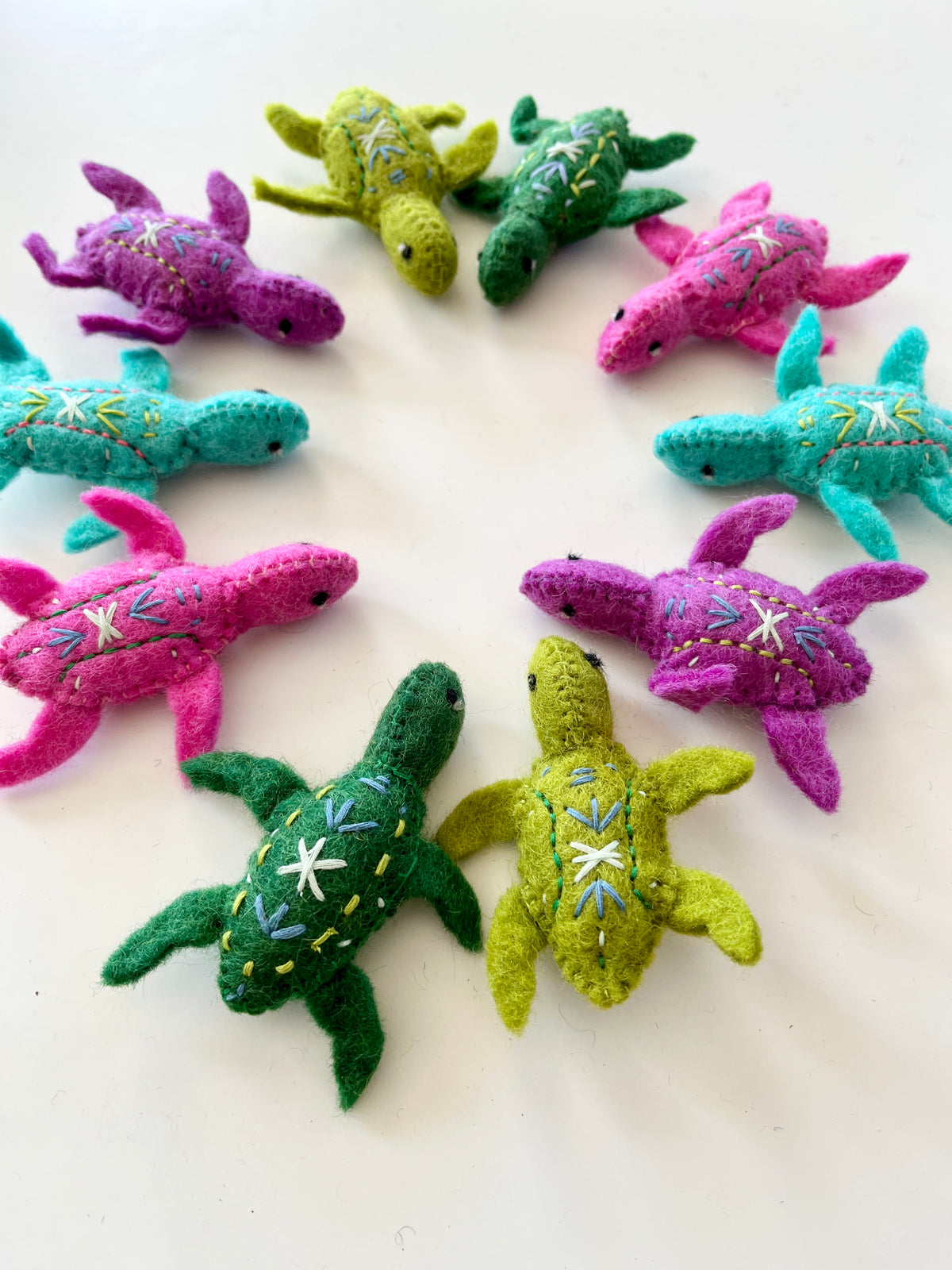 Colorful handmade felt turtles with embroidered details arranged in a circle on a white surface