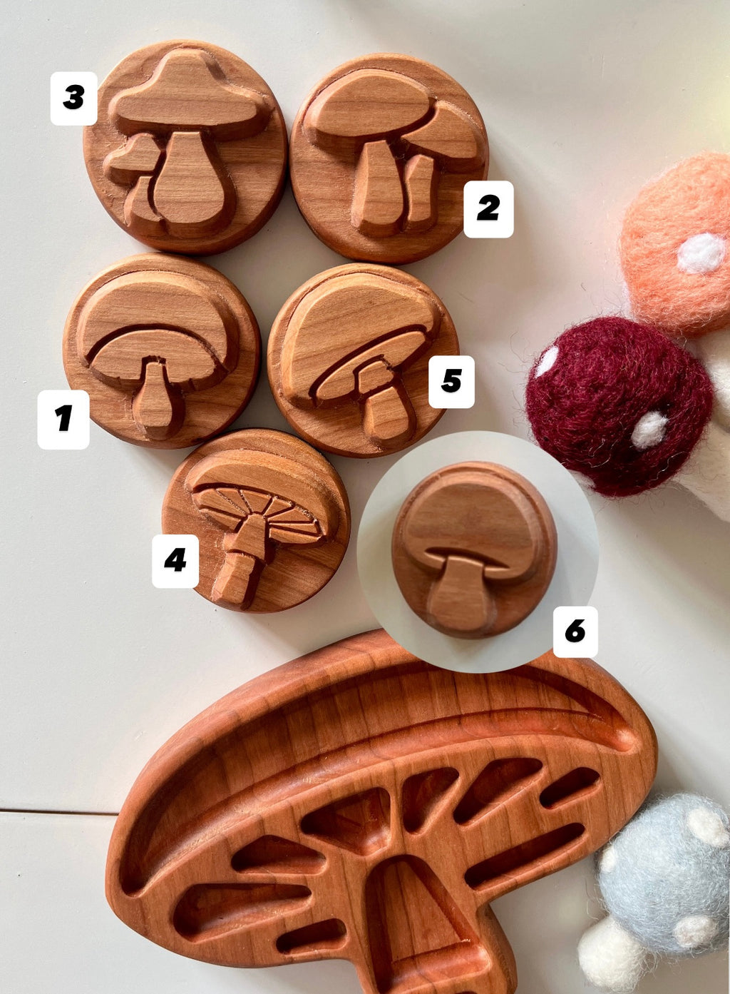 Set of six round wooden mushroom stamps with carved mushroom designs alongside felt mushroom toys on white surface