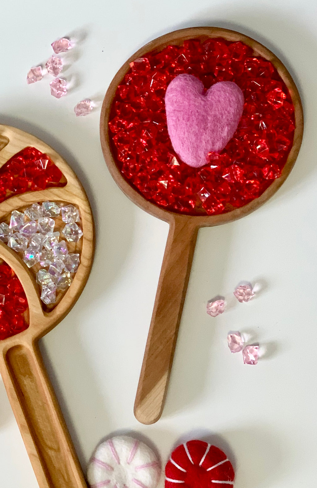 Wooden handheld sensory tray filled with red acrylic gems and pink felt heart on white background