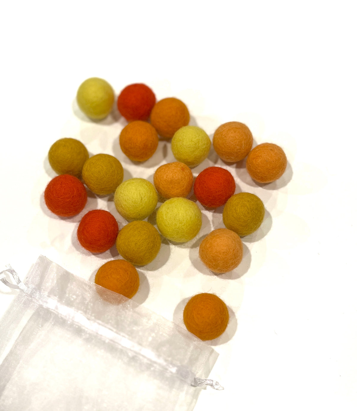 Assorted wool felt balls in shades of orange, yellow, and red scattered near a sheer white drawstring bag