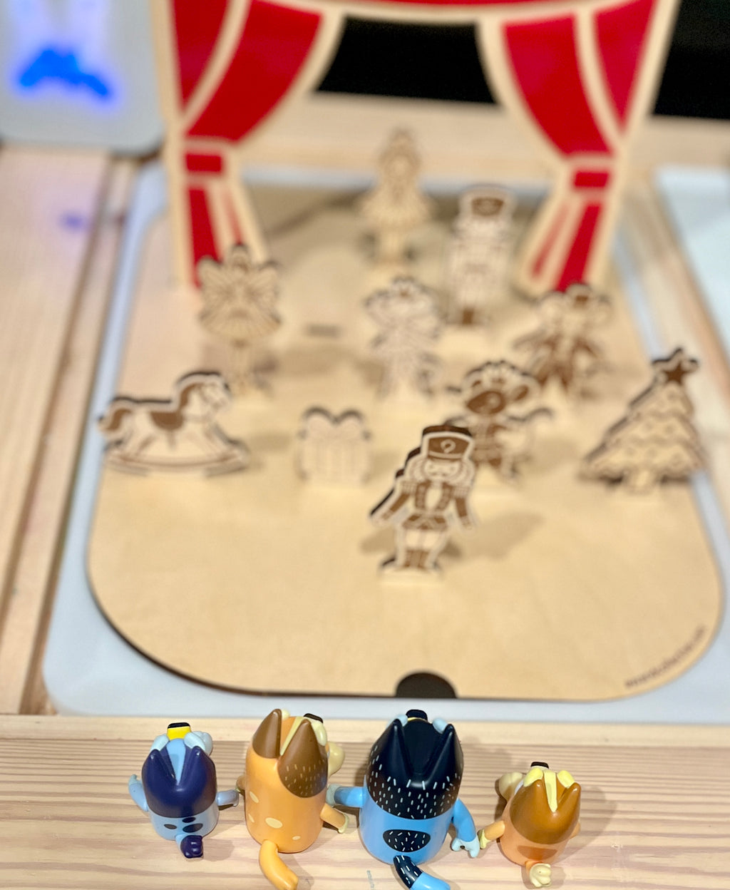 Four small animal figurines facing a wooden stage with holiday-themed laser-cut characters and red curtains