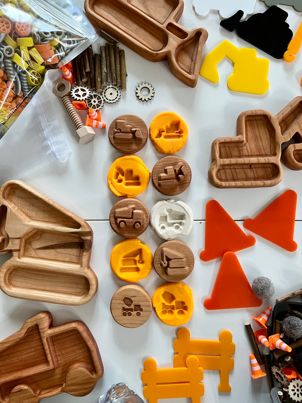 Wooden and colorful construction vehicle-shaped molds, small gears, sticks, and traffic cones on a white surface
