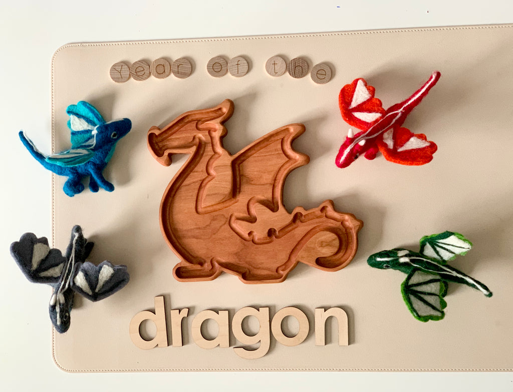 Wooden dragon-shaped tray surrounded by hand-stitched felt dragons in blue, red, black, and green on beige surface