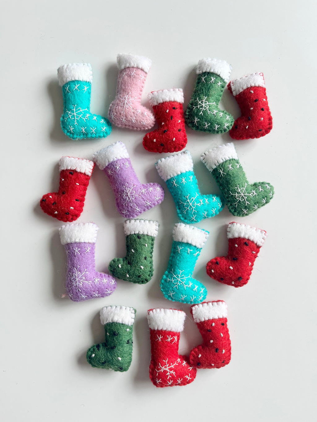 Felt mini Christmas stockings in red, green, blue, purple, and pink with white cuffs and stitched snowflake designs on white background