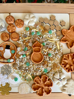 Wooden winter-themed trays and felt decorations arranged around a central pile of mixed beads and snowflake-shaped pieces