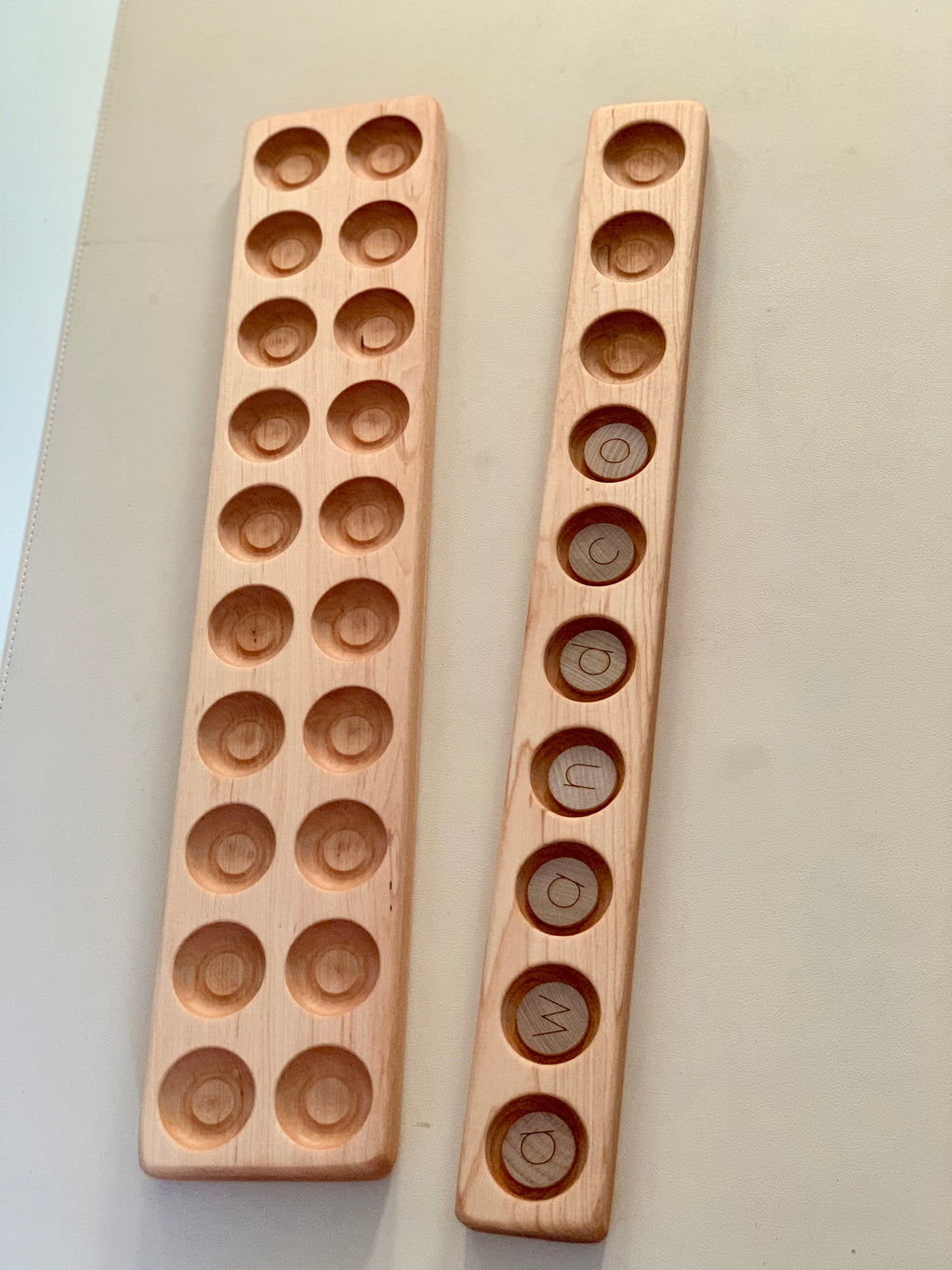 Two wooden trays with circular indentations on a beige surface, one featuring engraved letters in each recess