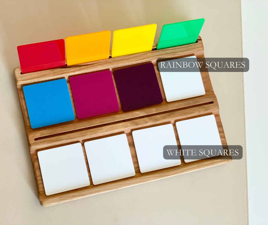 Wooden board holding colorful translucent squares in rainbow and white colors arranged in rows on beige surface