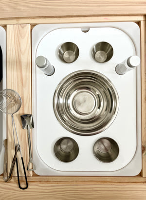 White tray with stainless steel bowls, spice shakers, and metal kitchen utensils on a wooden surface