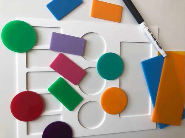 White board with colorful magnetic shapes including circles and rectangles and a black dry erase marker