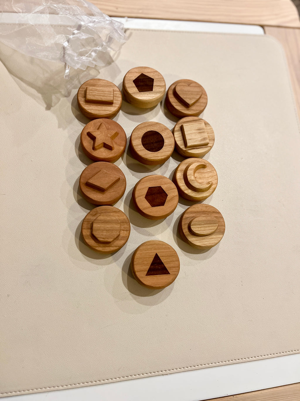 Set of wooden discs with various carved geometric shapes arranged on a beige surface next to a sheer white bag