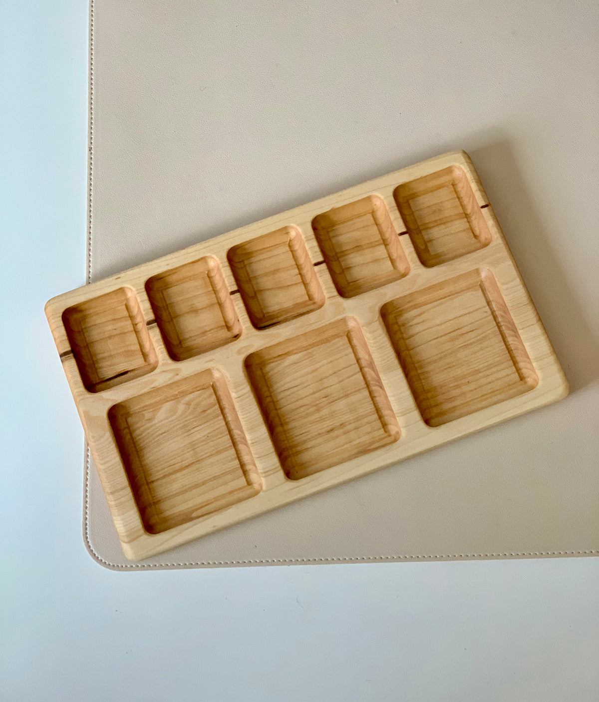 Rectangular wooden tray with eight compartments of varying sizes on a light beige surface