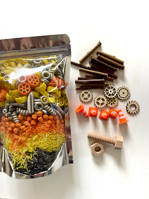 Clear pouch with multi-colored pasta, wooden twigs, gears, nuts, wooden screws, and orange traffic cones on white surface
