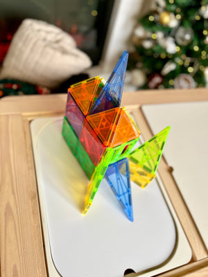 Colorful translucent magnetic building tiles assembled into a geometric house shape on white board with blurred background