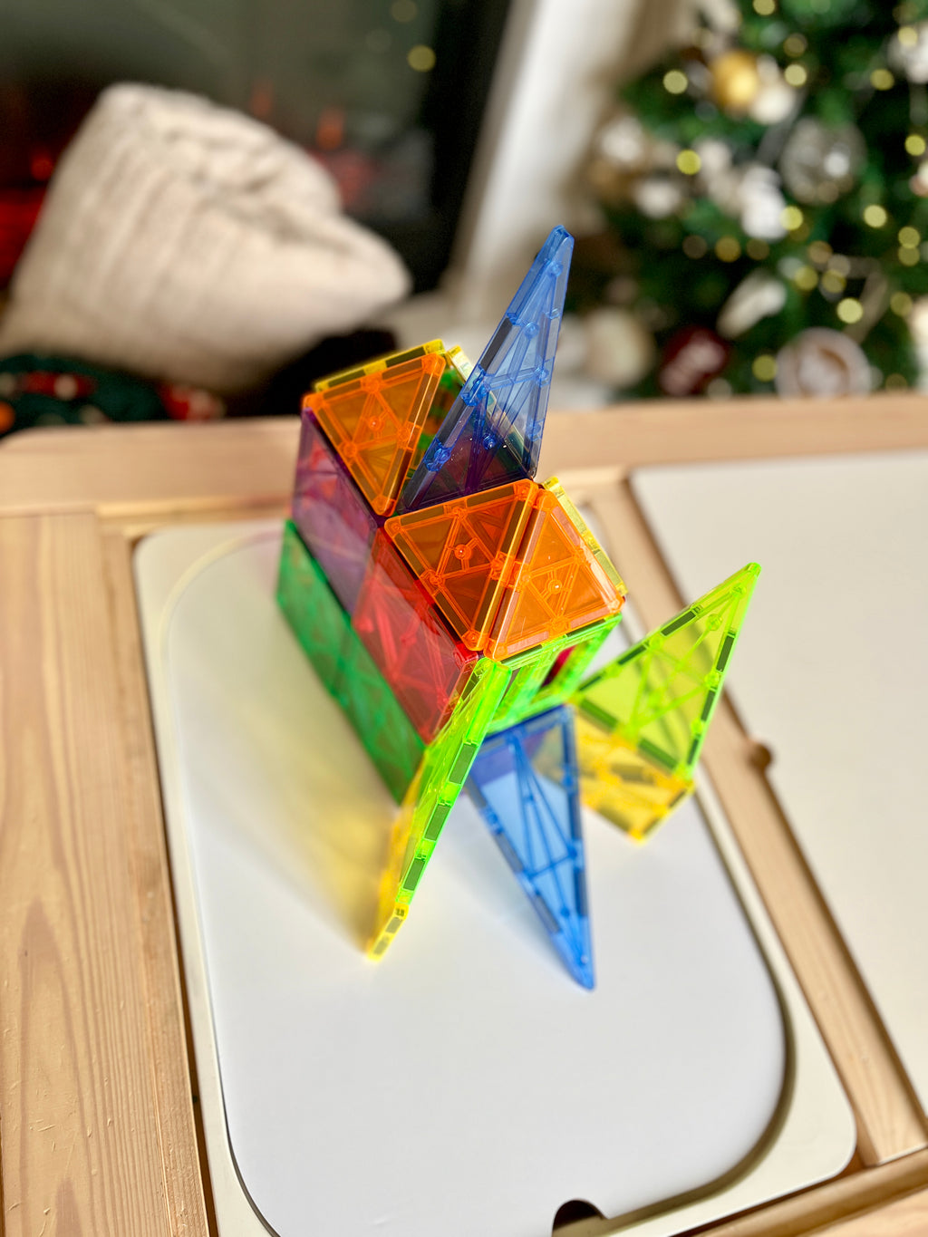Colorful translucent magnetic building tiles assembled into a geometric house shape on white board with blurred background