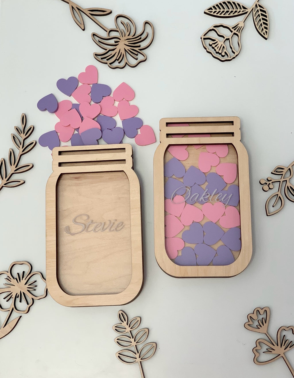 Two personalized wooden reward jars with pink and purple heart tokens surrounded by wooden floral cutouts on white surface