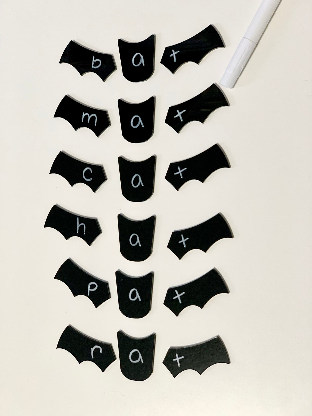 Black bat wing and center-shaped chalkboard labels with white handwritten words bat, mat, cat, hat, pat, rat on white surface