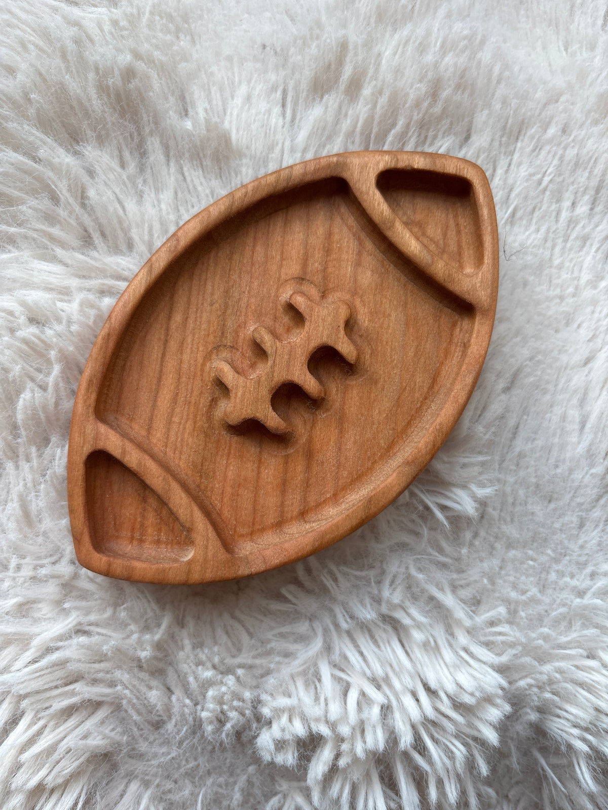 Smooth wooden tray carved in the shape of a football with lace details on a soft white fur surface
