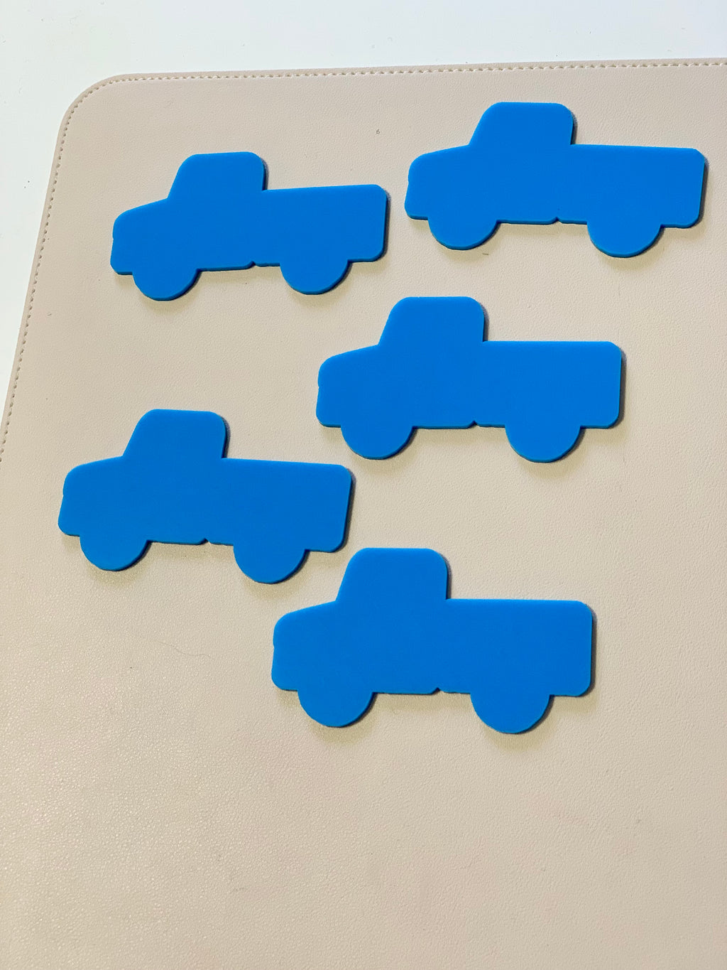 Five flat blue truck-shaped cutouts arranged on a light tan surface with stitched edges
