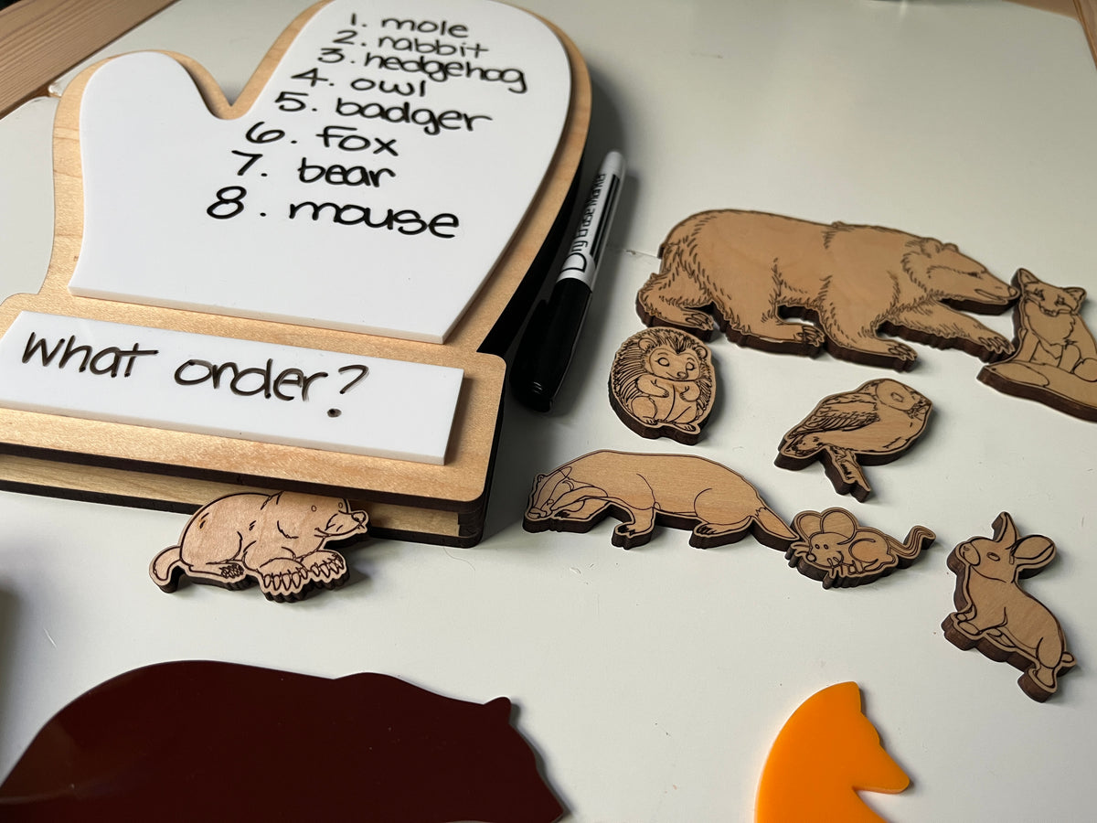 The Mitten Wooden Animals and/or Little Dry Erasables with Mitten Interactive Learning Set featuring handcrafted wooden animal pieces arranged beside a white dry-erase mitten board with handwritten animal names, a dry-erase marker, and a wooden tray, unique homeschool education resources.