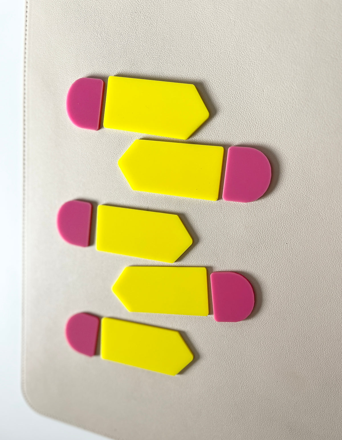 Five yellow arrow-shaped plastic tags with rounded pink ends arranged on a smooth light surface