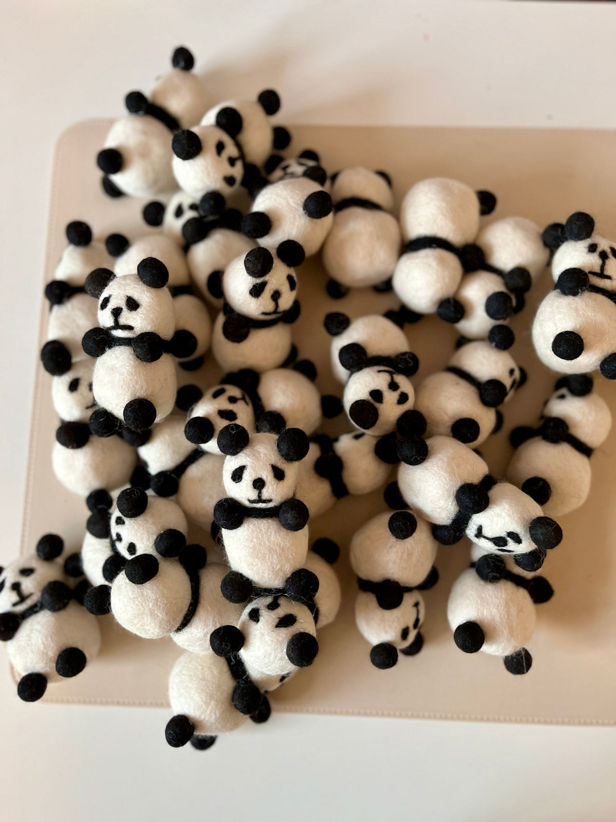 Cluster of small handmade felt panda figures with black ears and simple facial features on a light surface