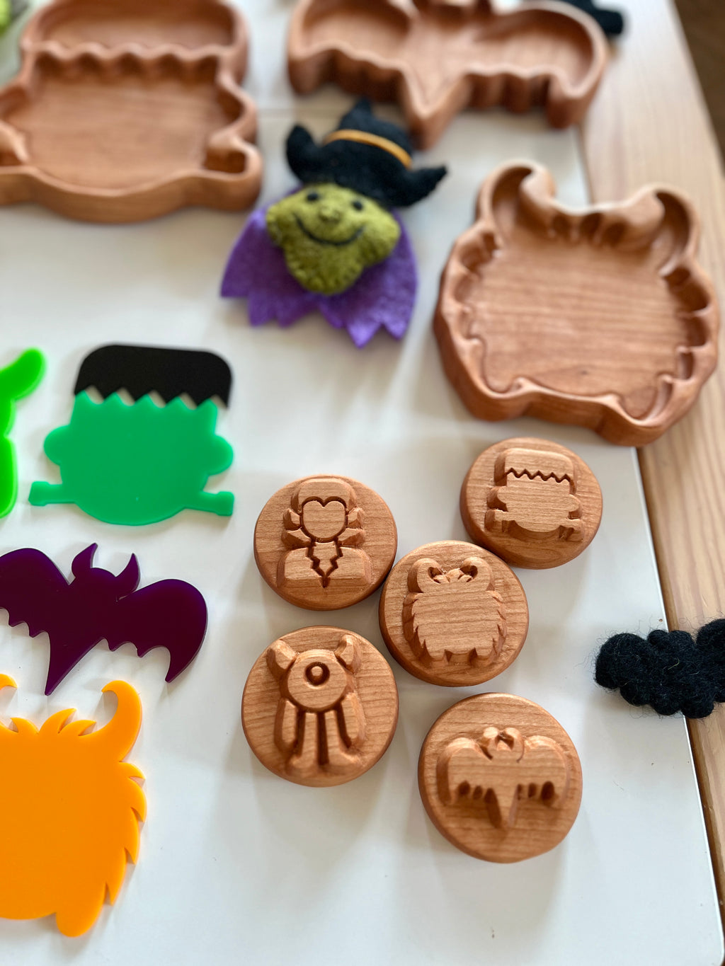 Round wooden tokens engraved with various Halloween monster faces alongside colorful acrylic monster shapes and wooden trays