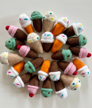 Assorted colorful felt ice cream cones with sprinkles and cherries arranged in a circular pattern on white background