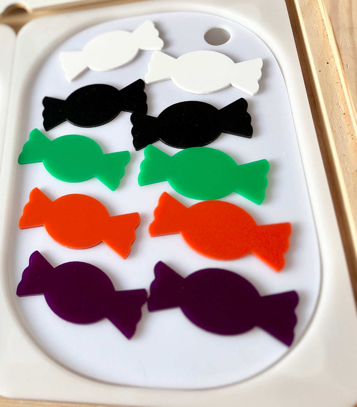 Eight candy-shaped cutouts in white, black, green, orange, and purple arranged in four rows on a white tray