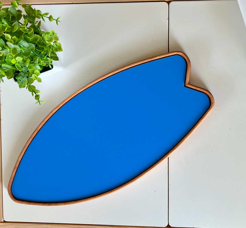 Blue surfboard-shaped tray with wooden edges on a white surface next to a small green plant