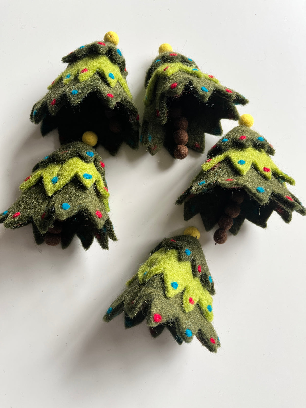 Felt miniature Christmas trees with layered green branches, multicolored dots, and small brown pinecone accents on white background