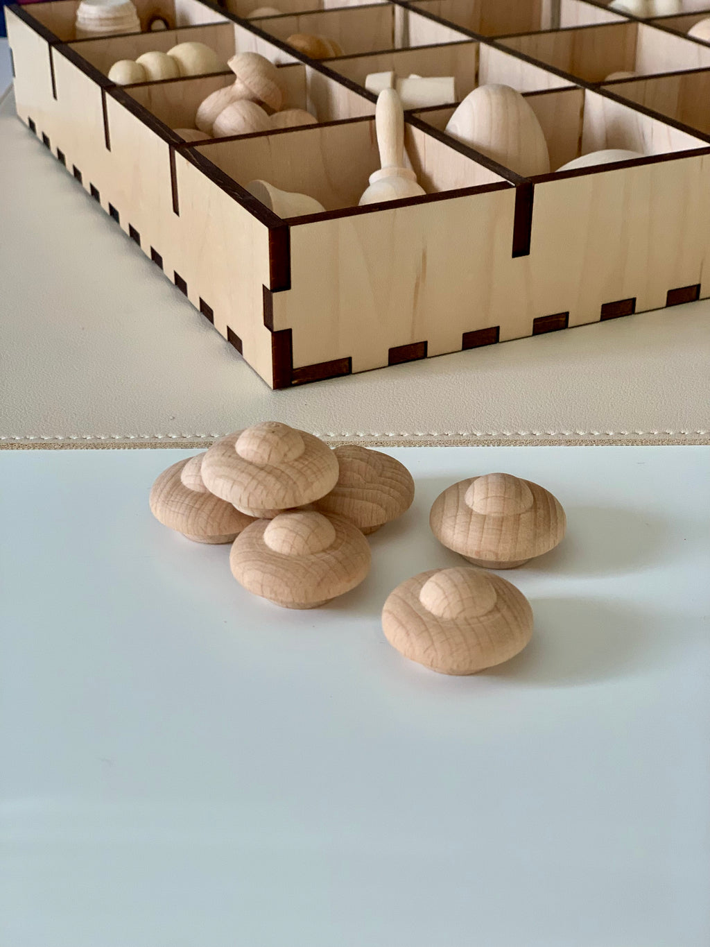 Six rounded smooth natural wooden shapes placed on a white surface with a divided wooden storage box in background