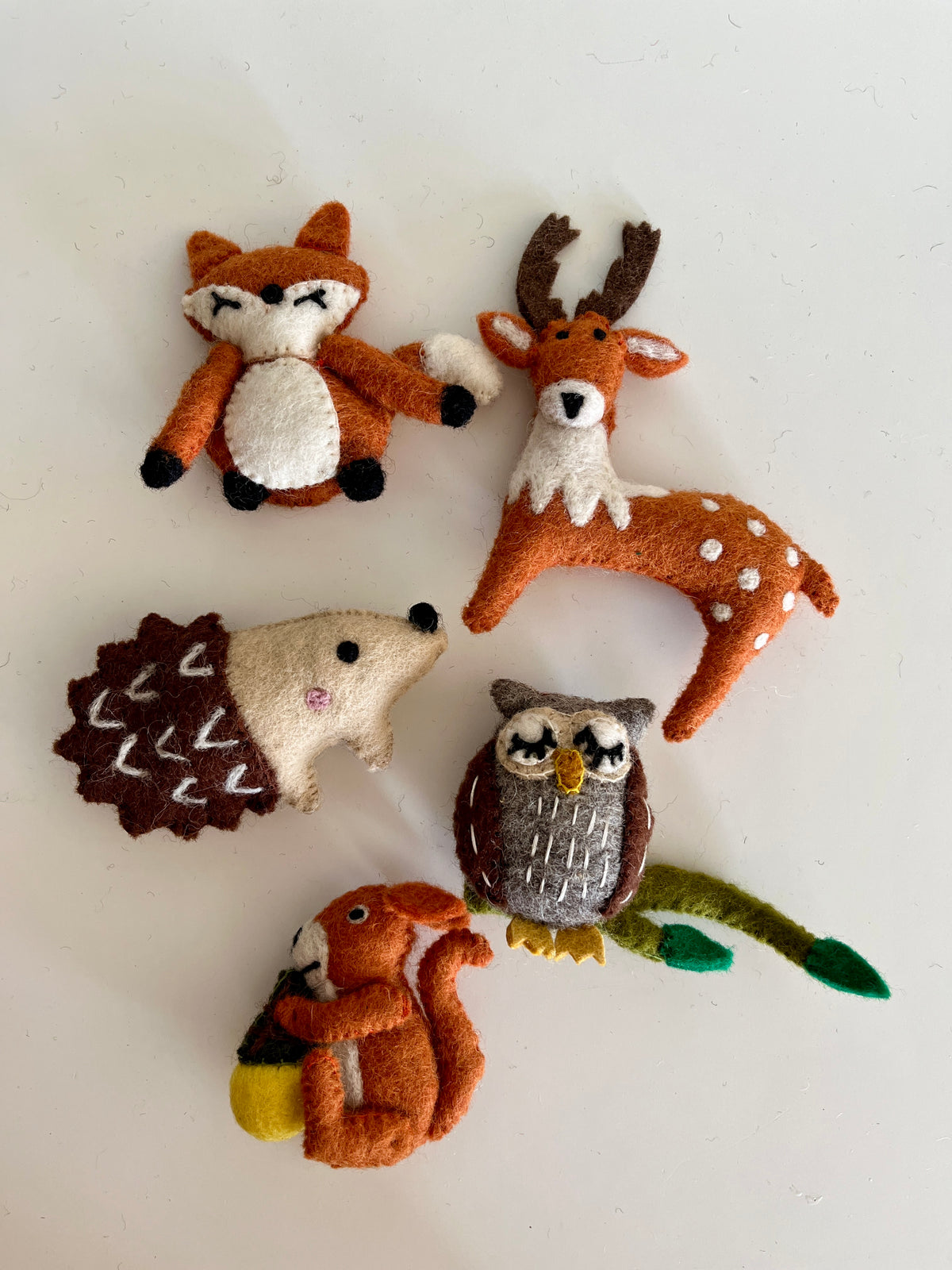 Five small handmade felt woodland animals including a fox, deer, hedgehog, owl, and squirrel holding an acorn on white background