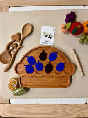 Wooden muffin-shaped tray with seven felt blackberries, wooden spoons, rolling pin, educational card, and felt fruit pieces nearby