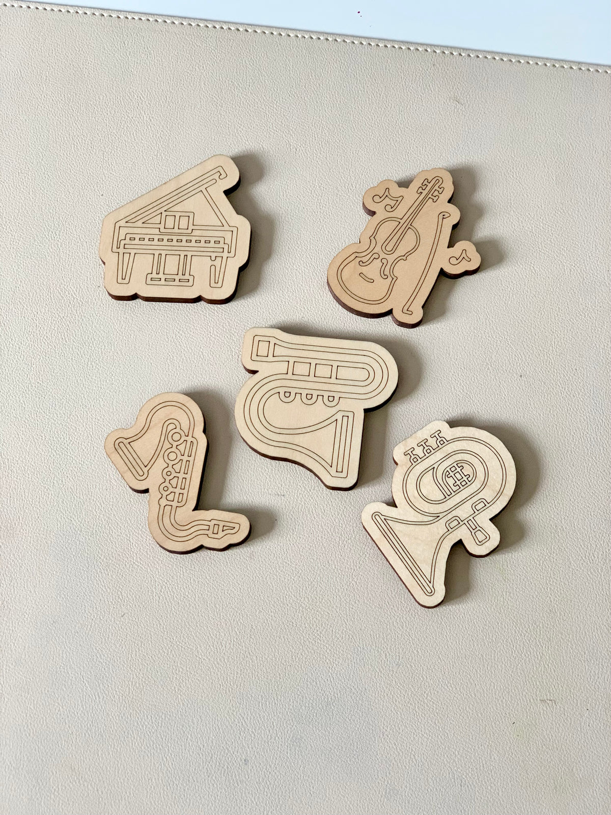 Five laser-cut wooden tokens featuring engraved grand piano, violin, saxophone, trumpet, and French horn designs on a light surface