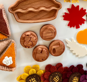 Carved wooden pie-shaped tray with circular wooden tokens featuring Thanksgiving-themed icons on white surface