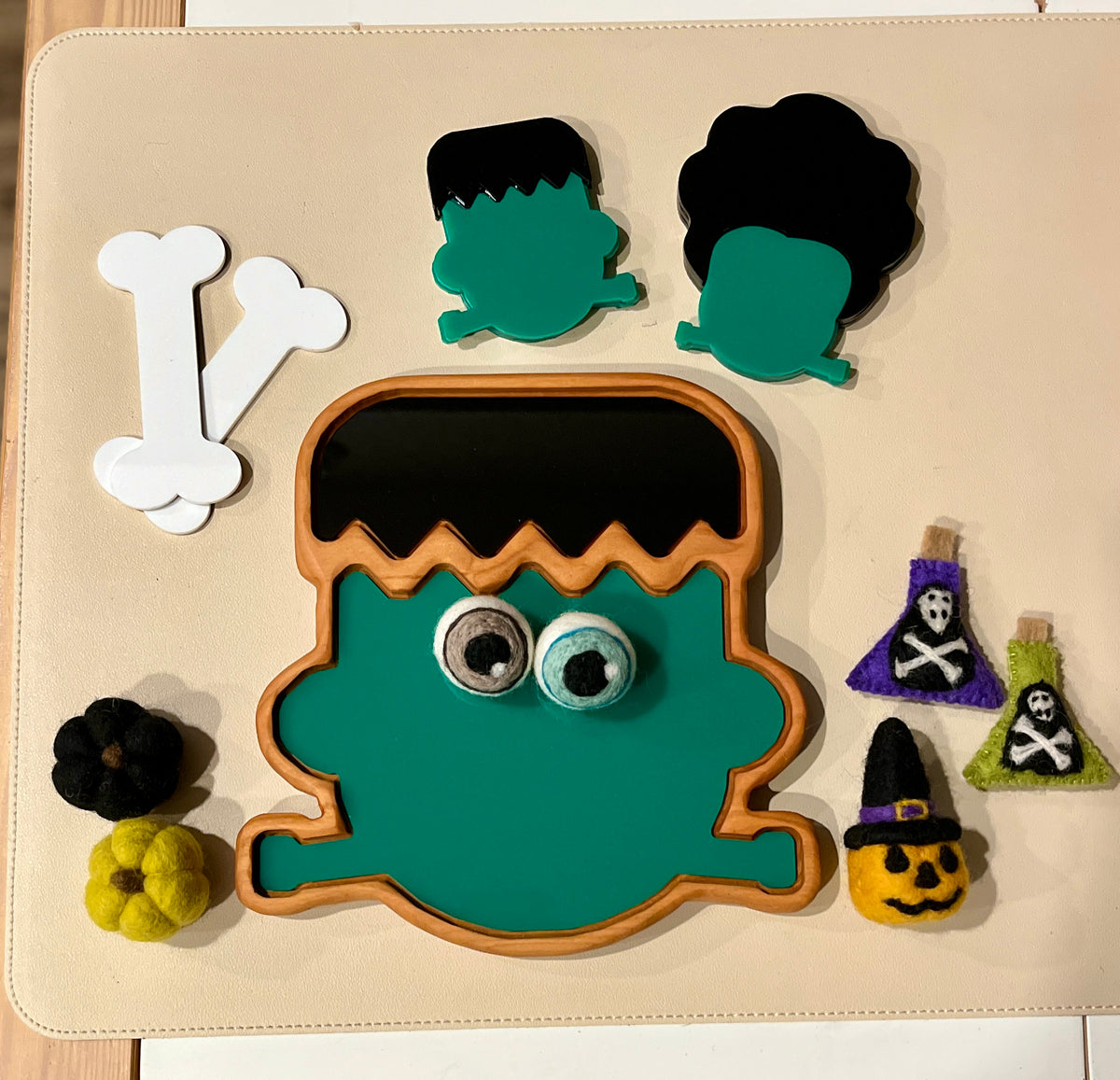 Wooden puzzle pieces and felt decorations featuring a green Frankenstein face, bones, pumpkins, and potion bottles on a beige surface